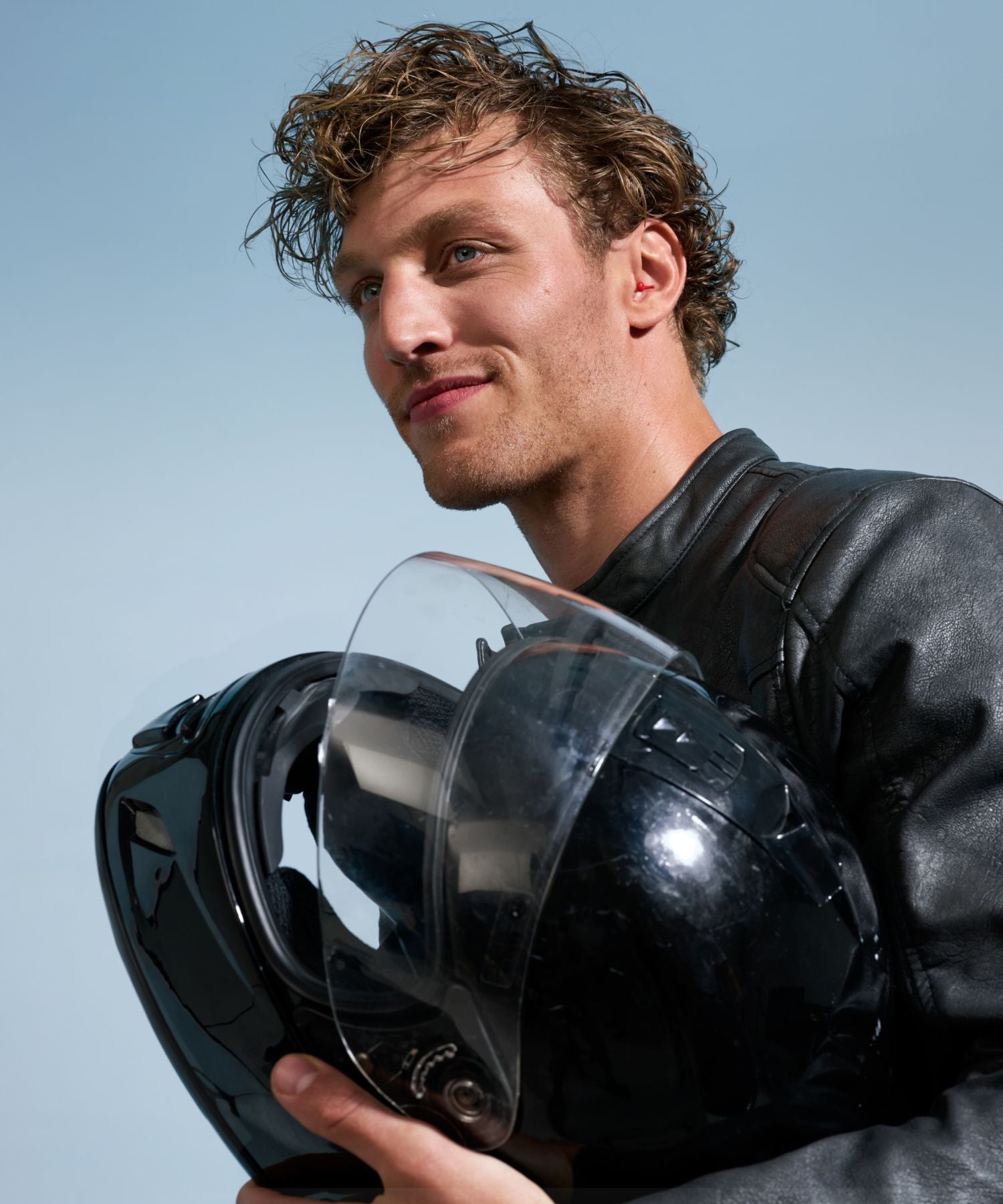 Un homme tenant un casque de moto et portant des bouchons d’oreille Alpine MotoSafe.