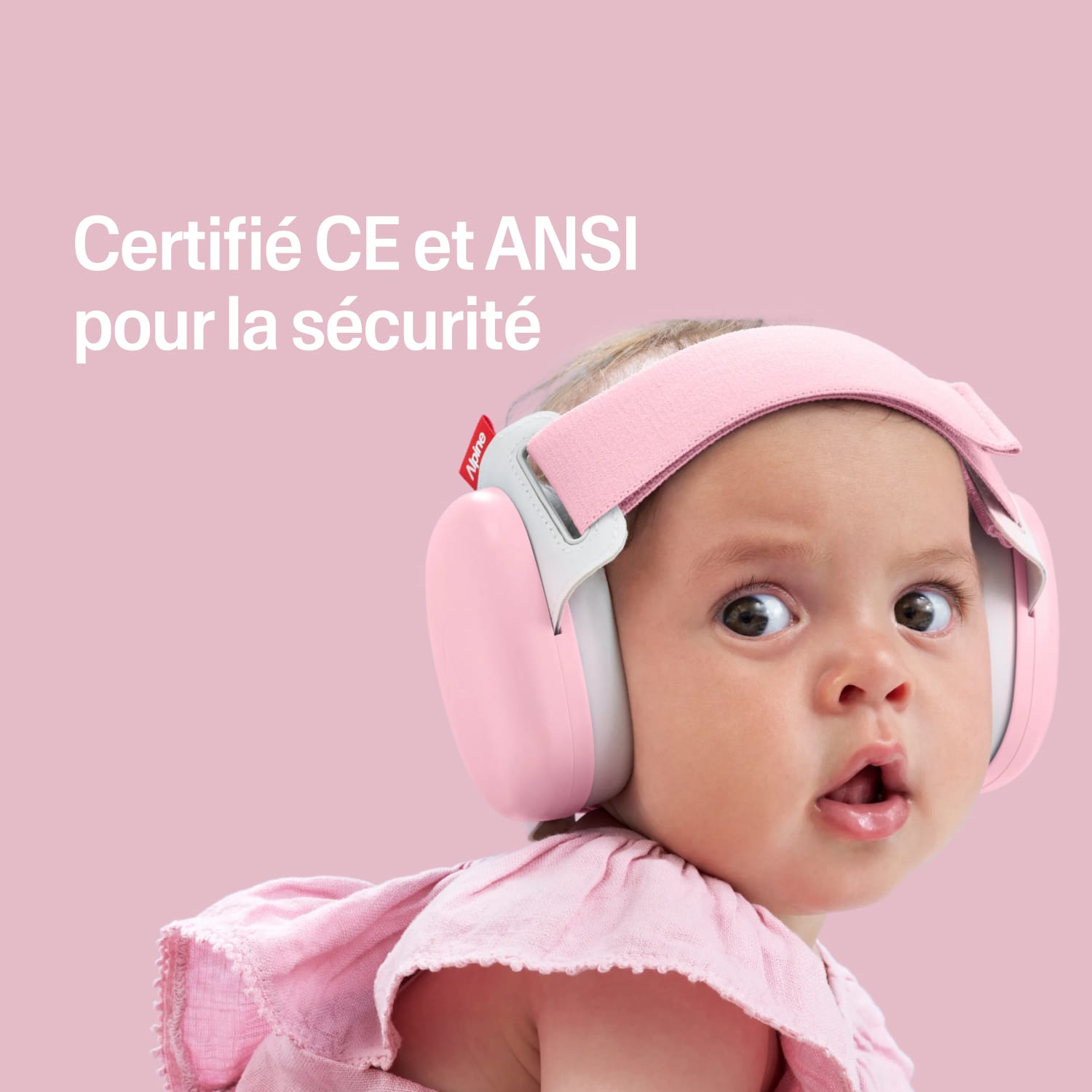 Baby wearing a pink muffy baby with certification text on a pink heart-patterned background