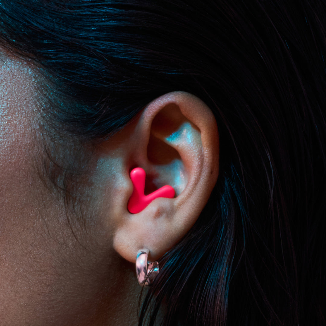 Detailed image of an ear with an Alpine Tune earplug in neon pink showing the snug fit in ear