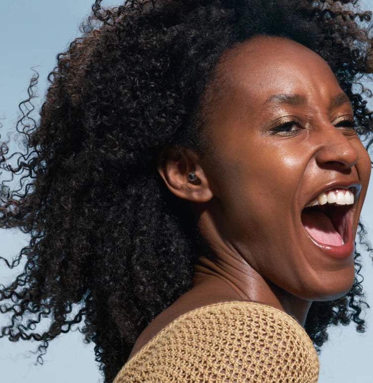 Een vrouw lacht terwijl ze Alpine-oordoppen draagt.