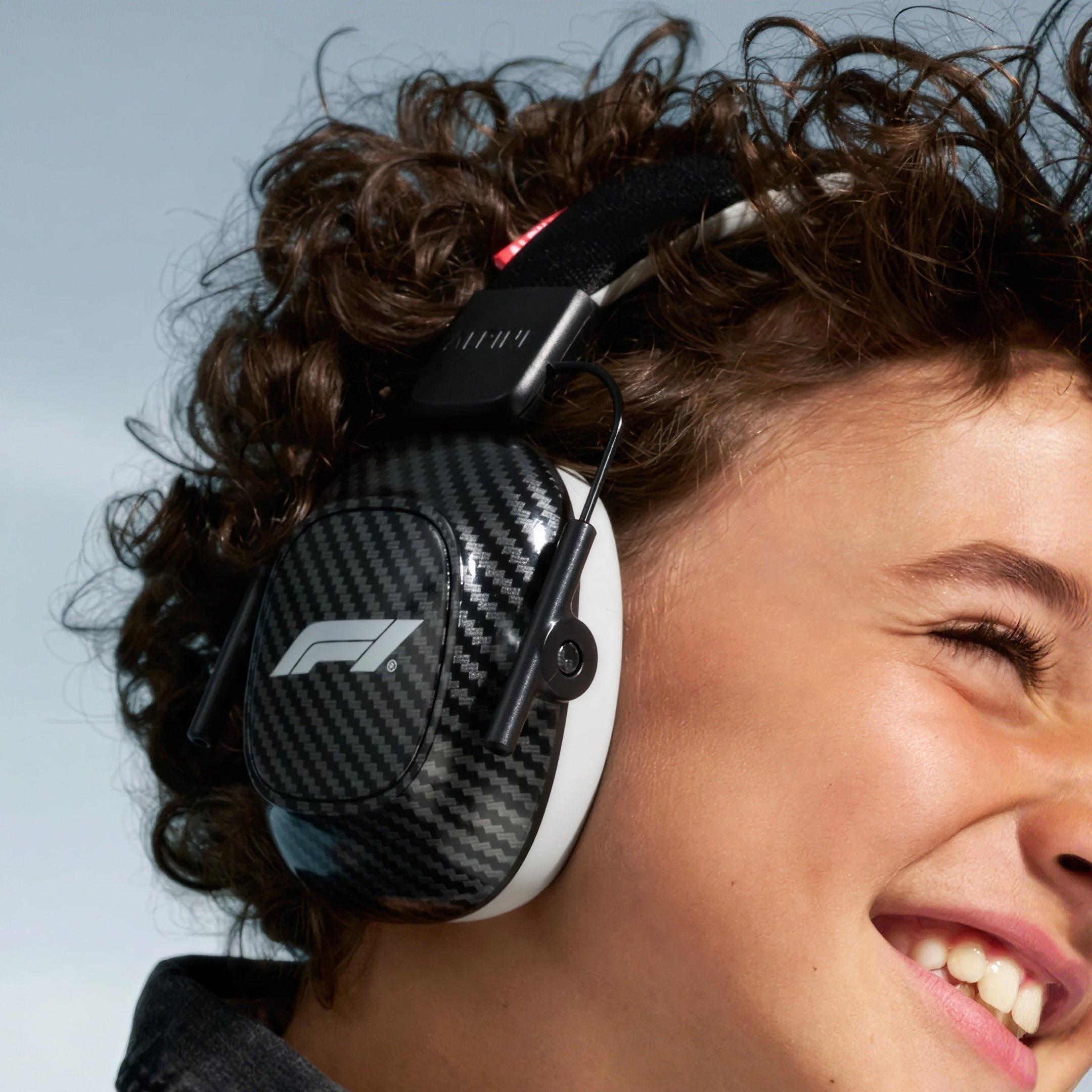 Smiling child with curly hair wearing Alpine Formula 1 Racing Muffy earmuffs
